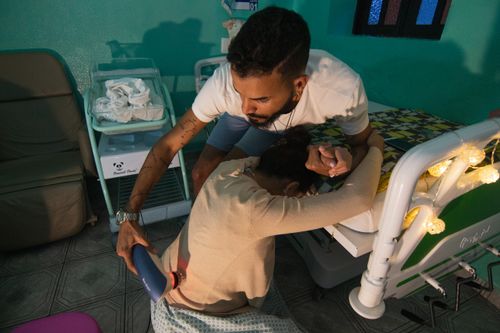 Free A man supports a woman in labor at a hospital bedside, holding her hand and using a device for comfort. Stock Photo