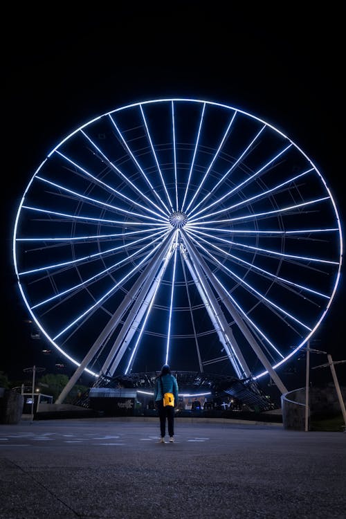 Woman Standing by Ferris Wheel at Night