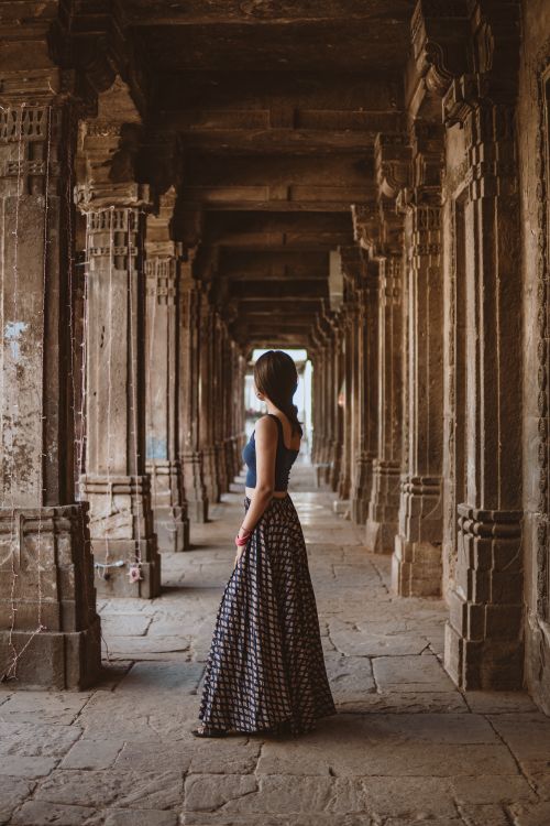 Free Woman stands gracefully in an ancient Indian stone corridor, showcasing a blend of fashion and history. Stock Photo