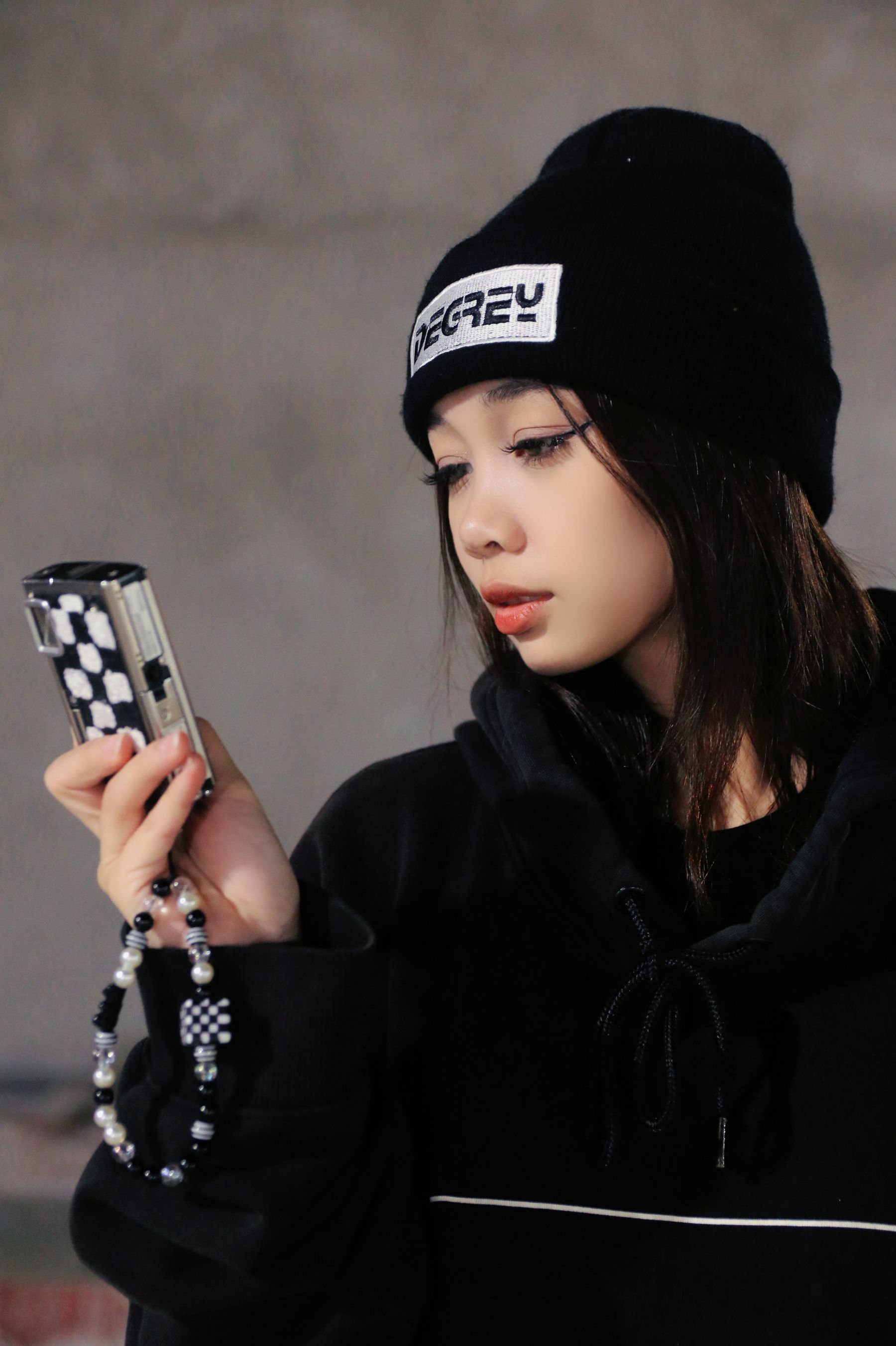 Young woman wearing a black beanie while checking a compact digital camera