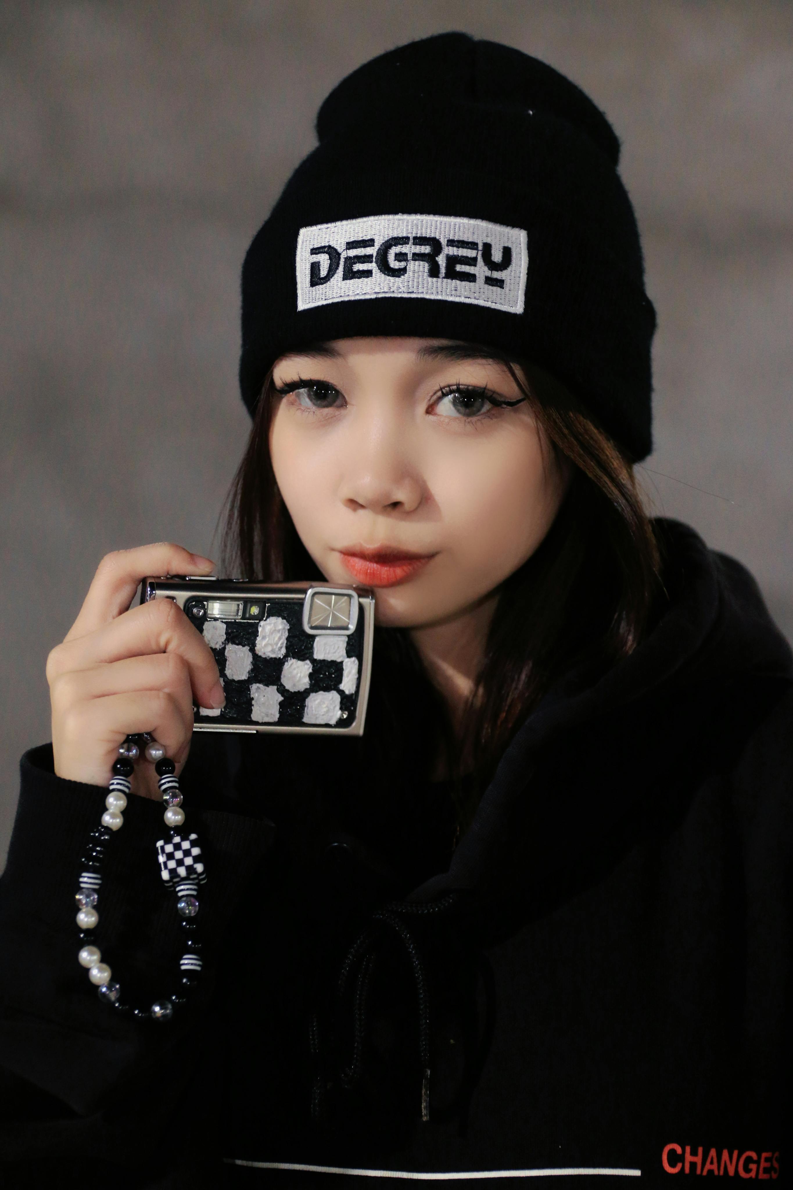 A portrait of a young woman in a beanie and hoodie holding a fashionable accessory.