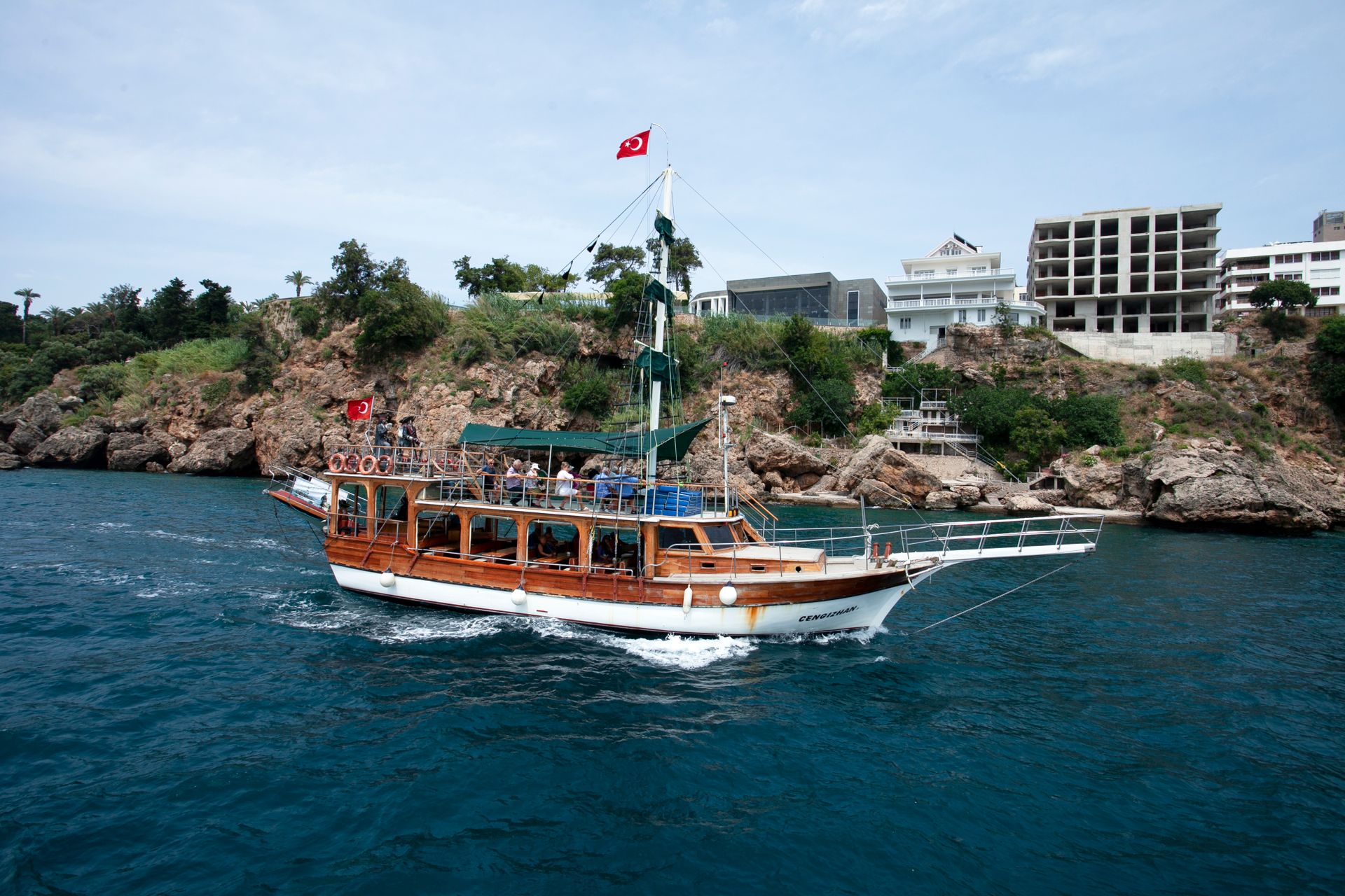 A traditional sailing boat glides along the Turkish coastline under a clear summer sky.