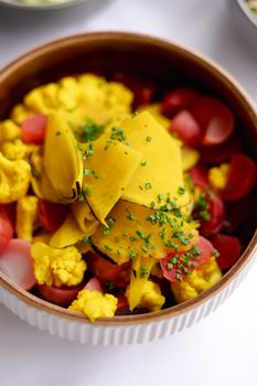 A bowl of colorful pickled vegetables including cauliflower, radish, and curried spices, garnished with chives.