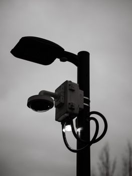 Atmospheric black and white photo of a street lamp with a security camera.