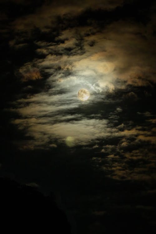 A full moon is seen through clouds in a dark sky