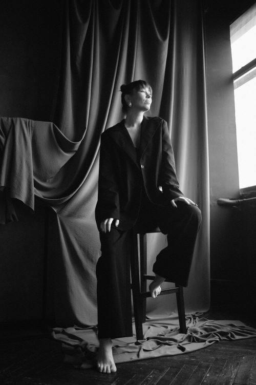 Free Artistic black and white portrait of a woman sitting on a high stool in a fashion studio setting. Stock Photo