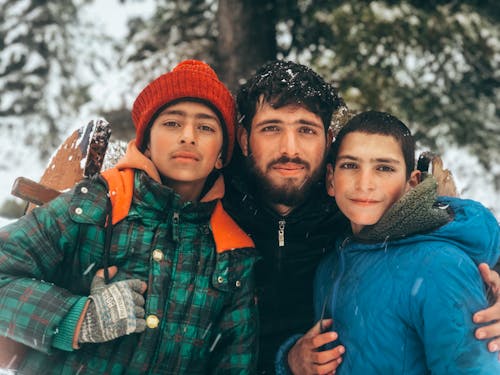 A Bearded Man and Two Boys in Jackets Standing Outside in Winter 