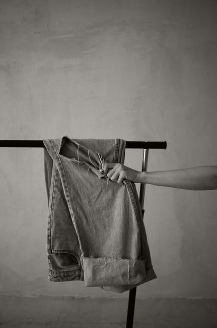 Minimalist black and white image of a hand gripping torn jeans on a rack indoors.