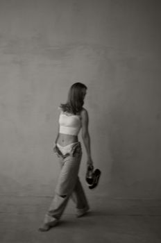 Grayscale photo of a woman in casual attire, barefoot and walking indoors.
