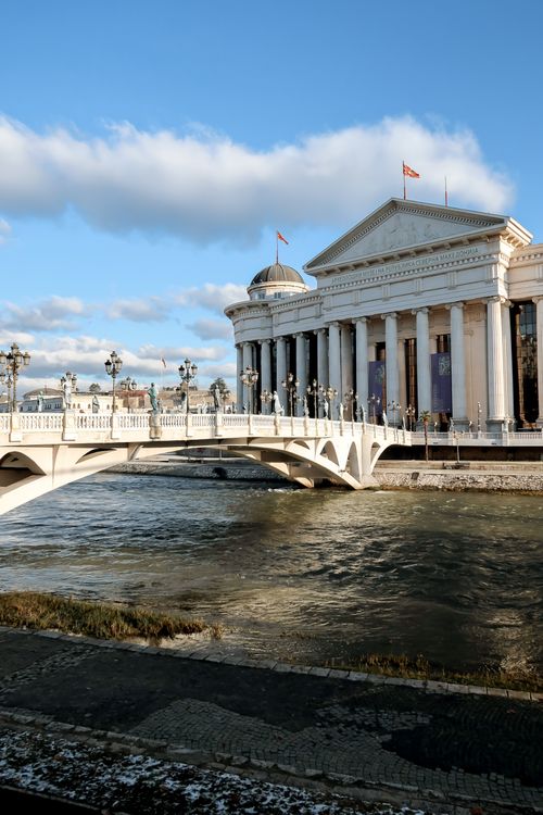 Free Elegant view of a neoclassical building and bridge over the Vardar River in Skopje, North Macedonia. Clear sky enhances the landscape. Stock Photo