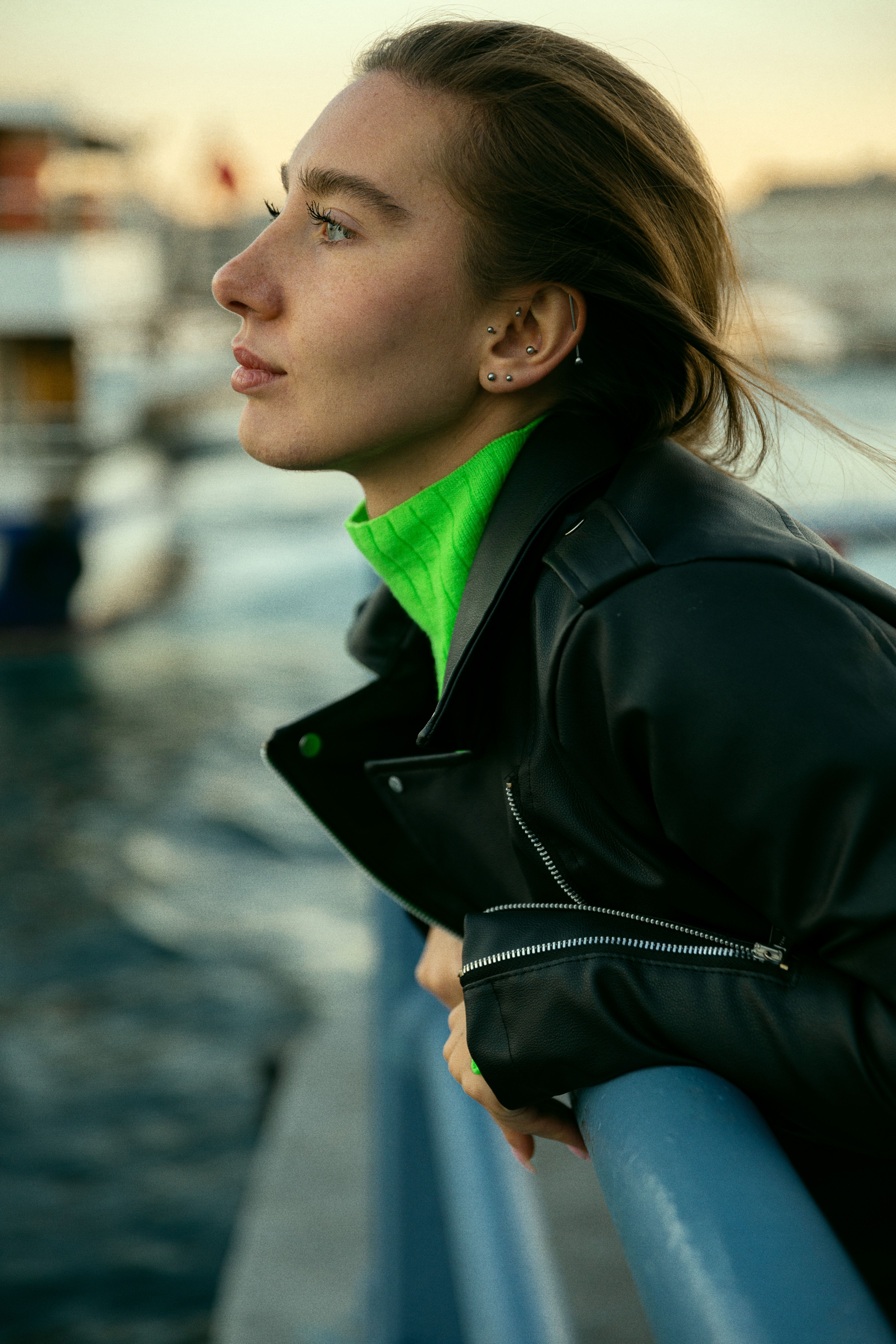 Profile of a woman in a leather jacket leaning on a railing with the sea in the background.