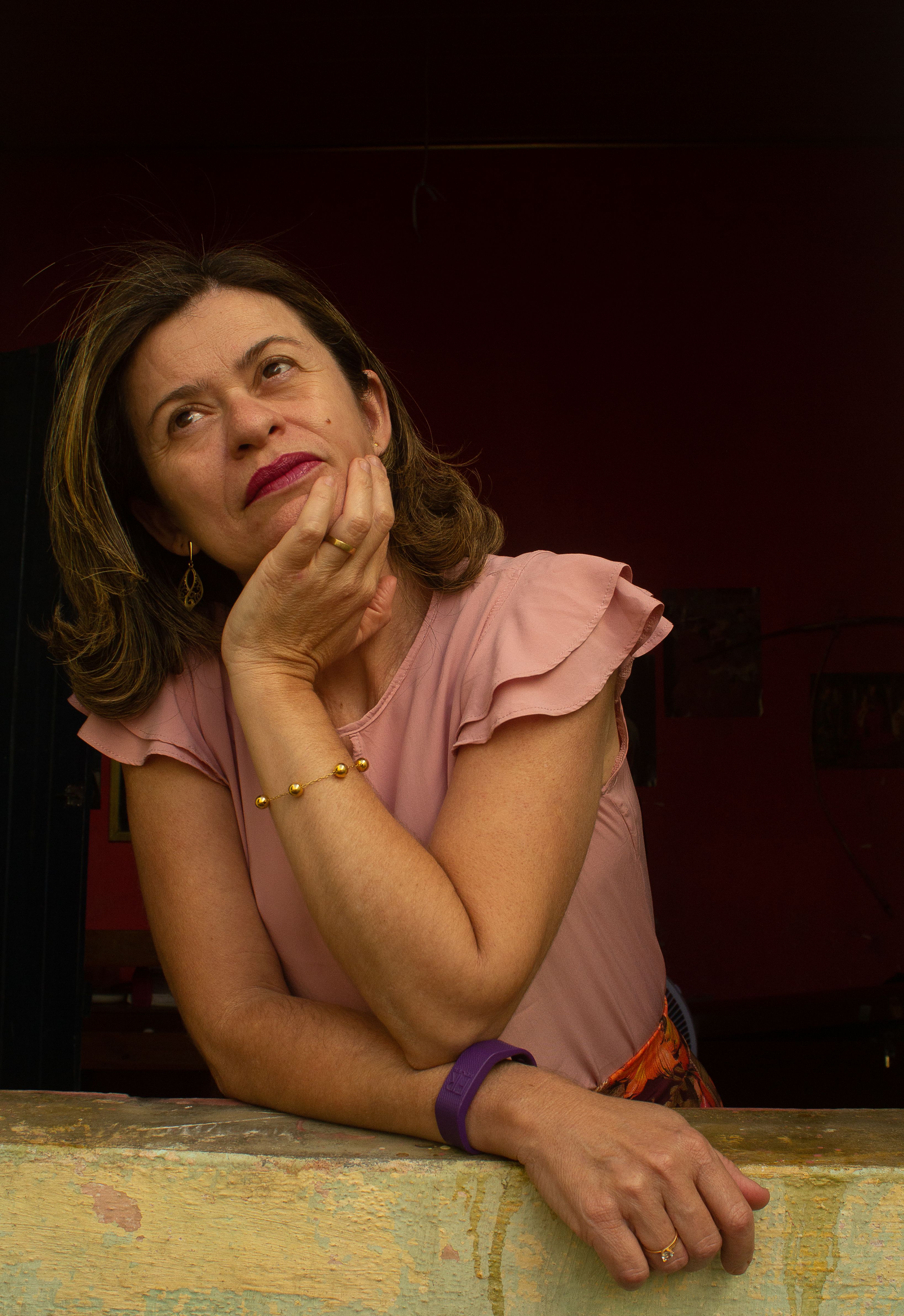 A thoughtful adult woman rests her chin on her hand, leaning on an indoor wall.