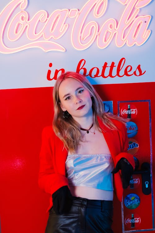 A young woman in a red leather jacket posing in front of a coca cola machine