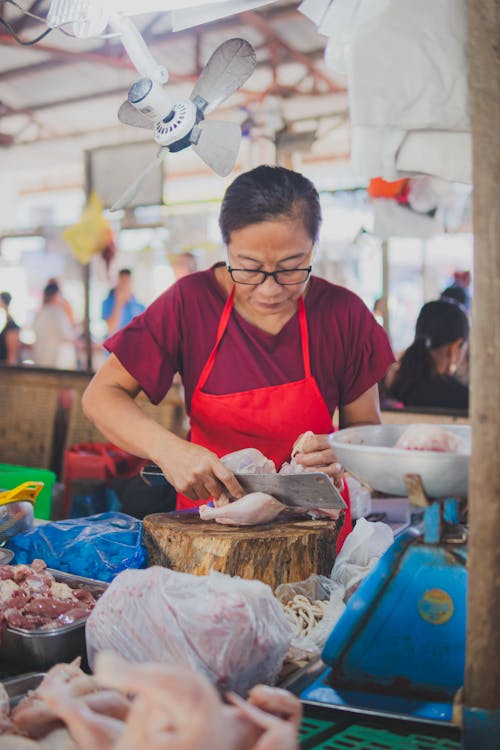 A woman in an apron cutting up meat at a market