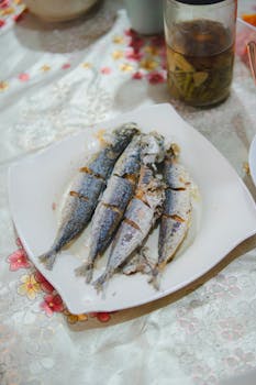Four fried fish served on a white plate with floral tablecloth. Perfect for food lovers.