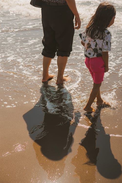 Man with Daughter Walking Barefoot at Beach