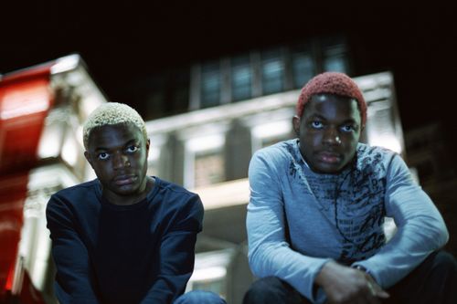 Free Two young men with vibrant hair posing at night in front of a lit building. Stock Photo