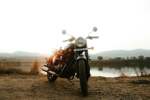 Free A parked Royal Enfield motorcycle by a tranquil lakeside at sunset, capturing nature's beauty. Stock Photo