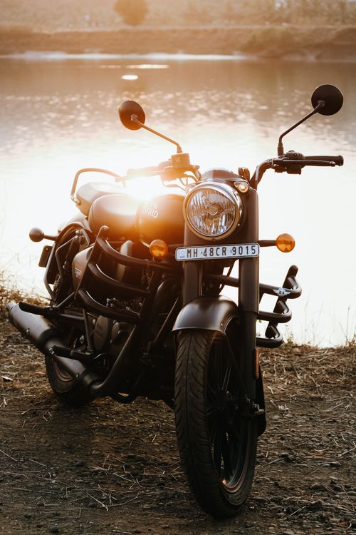 Free A classic motorcycle parked by a calm lake with a stunning sunset reflecting on the water. Stock Photo