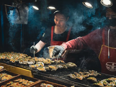 Vendors grilling seasoned oysters at a bustling night market stall.