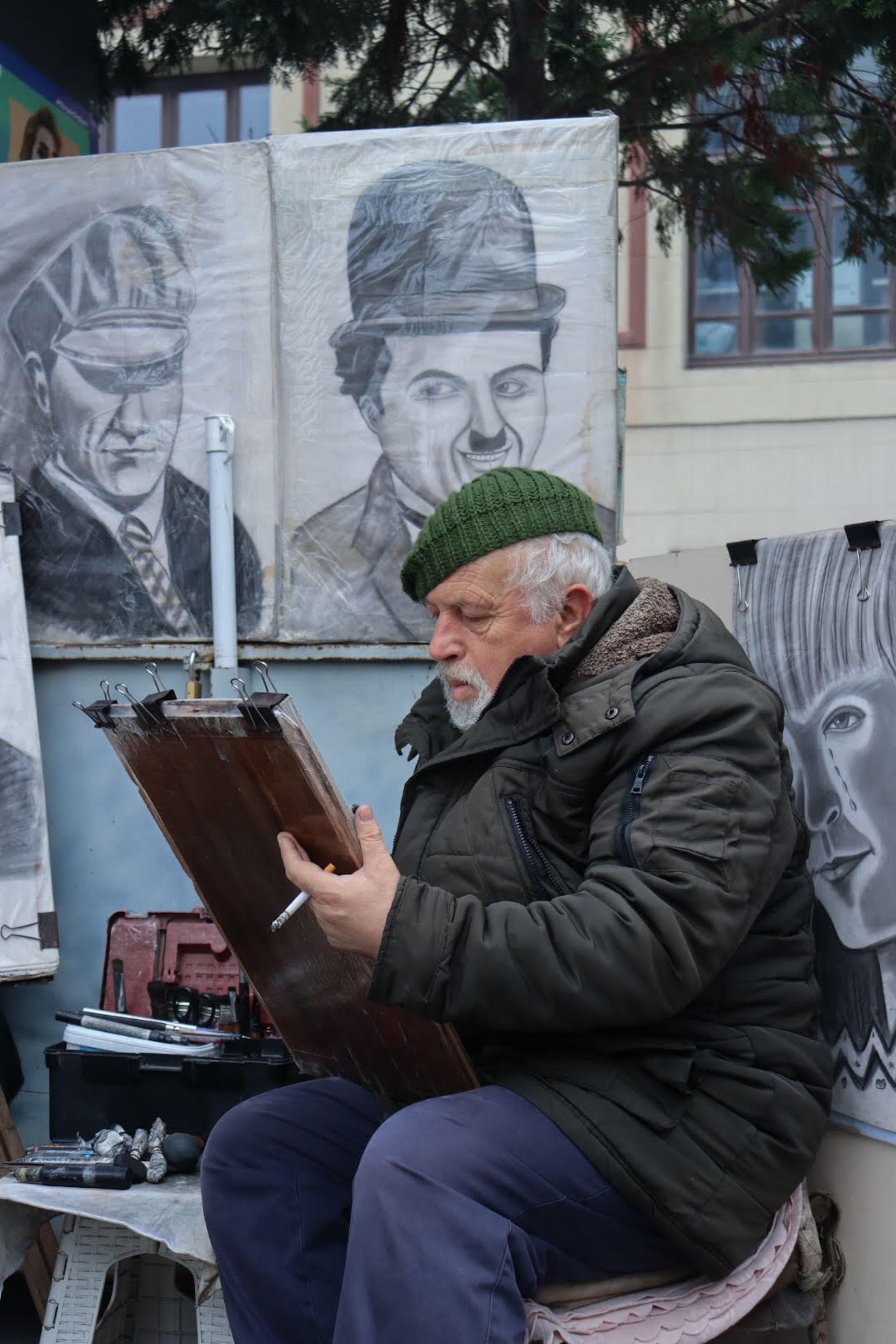 A street artist captures a portrait amongst charcoal sketches, adding life to urban art.