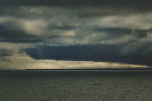 Free A moody seascape with a dramatic overcast sky reflecting in calm waters. Stock Photo