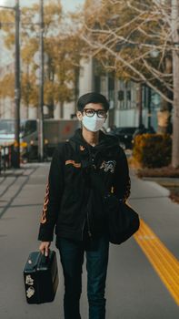 Young man with eyeglasses and face mask walks through Tokyo street, carrying luggage.