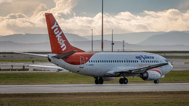 Air North passenger aircraft on the runway during sunset with scenic mountain backdrop.