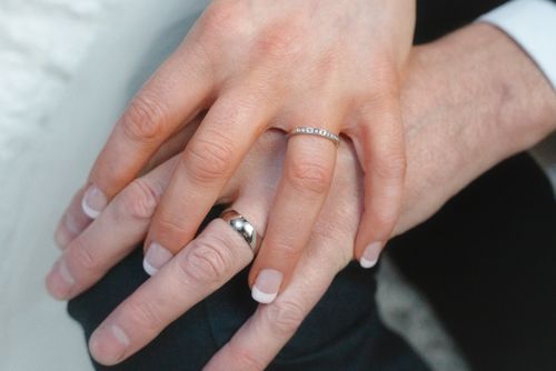 Free A romantic close-up showing a couple's interlocking hands with elegant wedding rings symbolizing love and commitment. Stock Photo