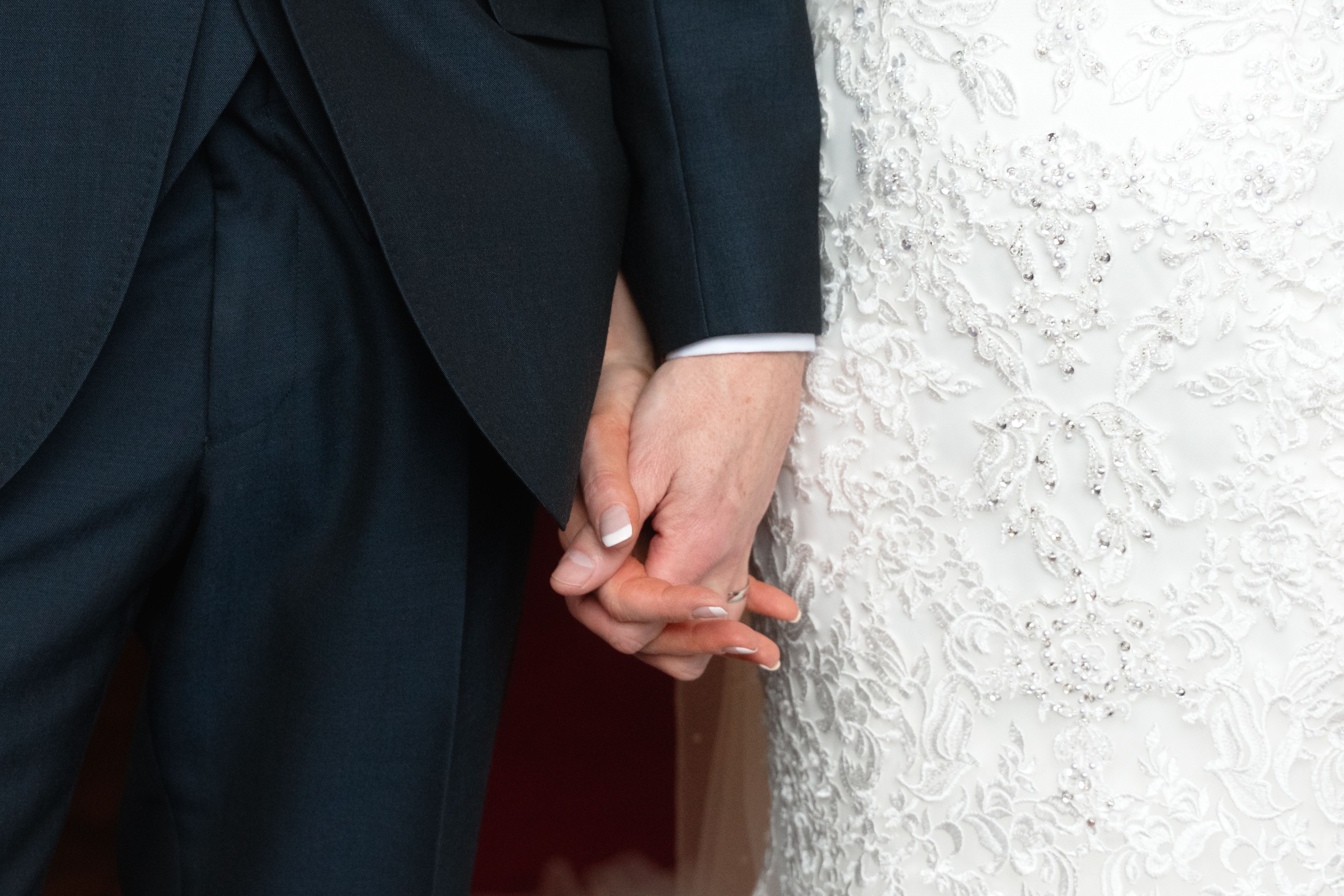 Close-up of a bride and groom holding hands on their wedding day.