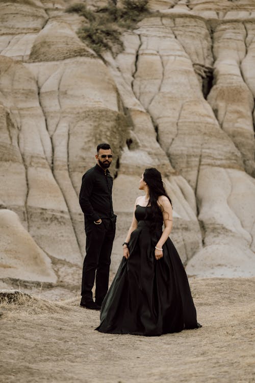 A couple in black dresses standing in front of a rocky landscape