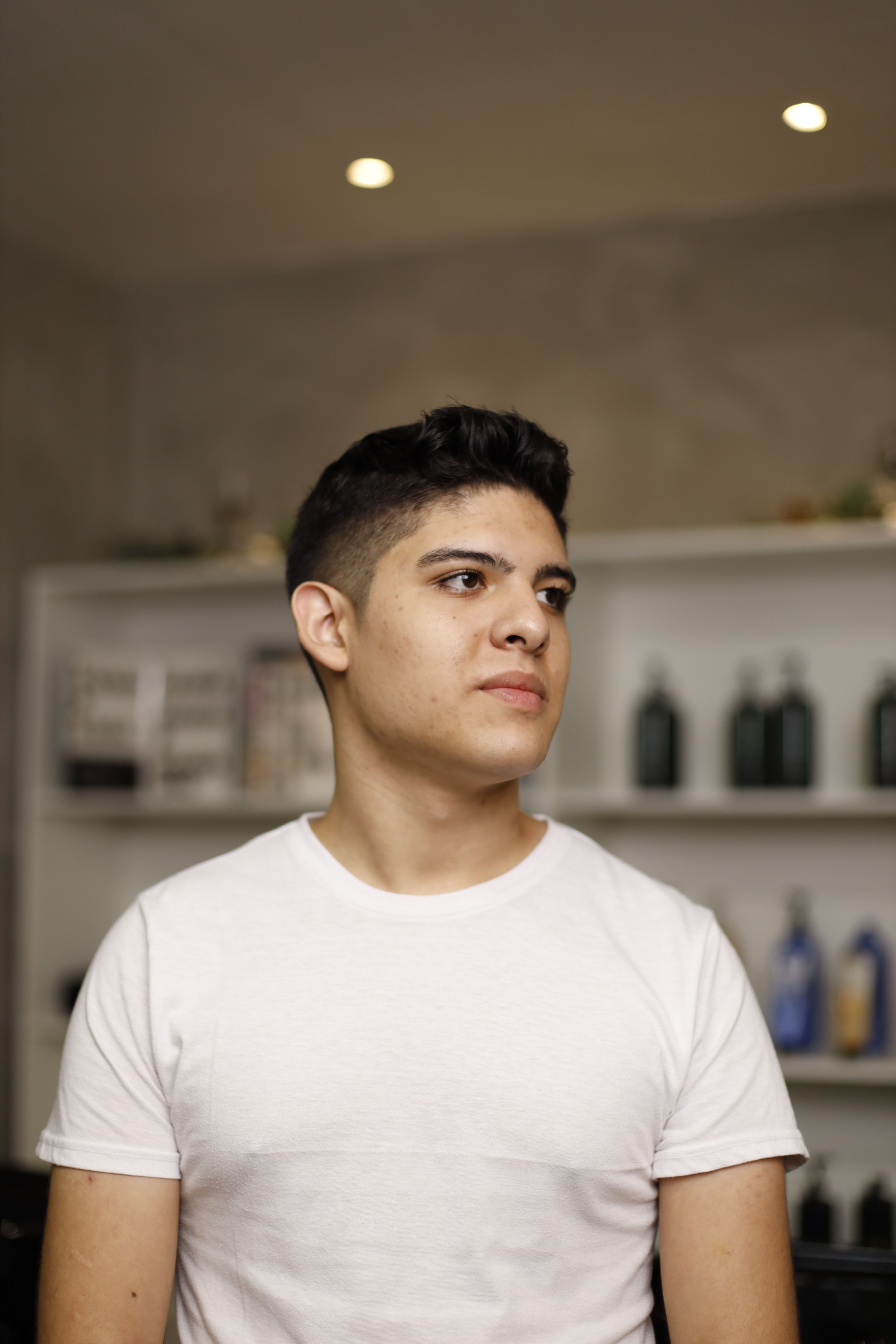 Portrait of a young man in a white t-shirt looking away indoors, shelves in background.