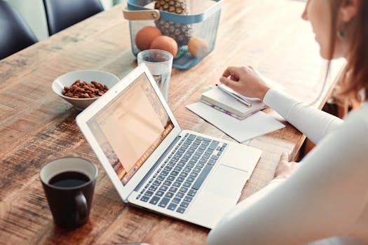 Woman working at home with a laptop, coffee, and healthy snacks on a wooden table.