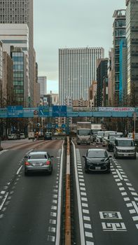 View of busy Tokyo street with skyscrapers and vehicles on a cloudy day.