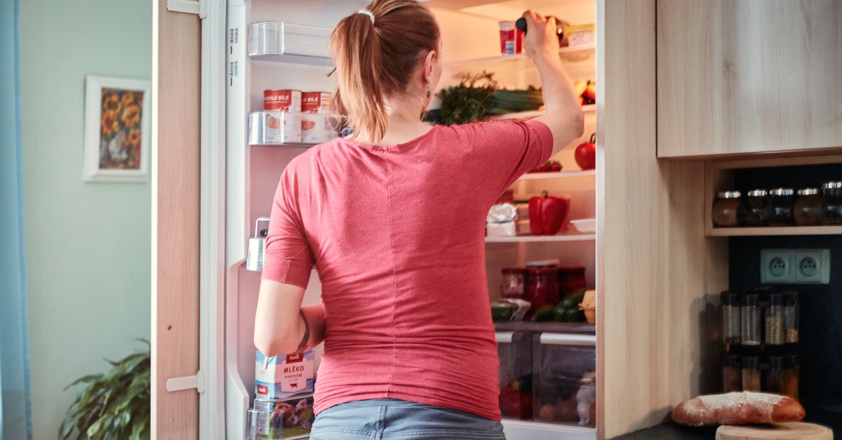 Uma mulher abre a geladeira para pegar itens alimentares em um ambiente de cozinha aconchegante.