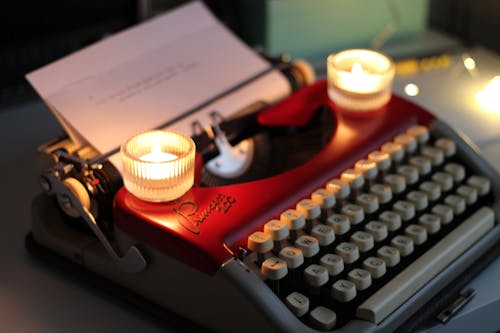 A red typewriter with two lit candles on it