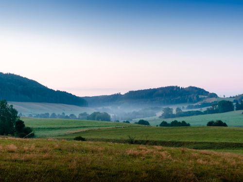 Free Explore the tranquil beauty of a rural landscape at dawn, featuring rolling hills and mist. Stock Photo
