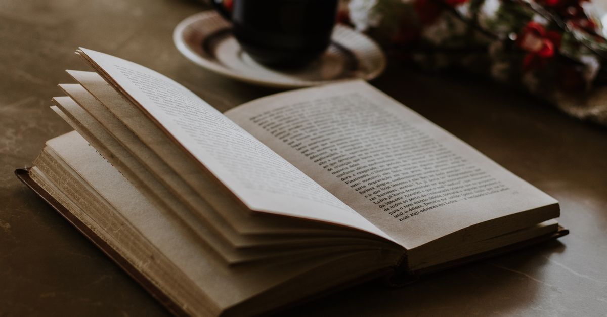 An open book lies on a table beside a coffee cup and flowers, offering a cozy reading ambiance.