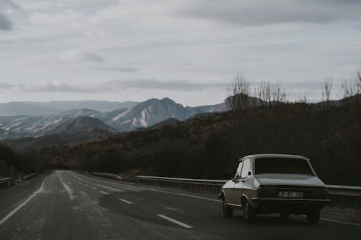 A classic car travels on an empty road with scenic mountain views, creating a nostalgic adventure feel.