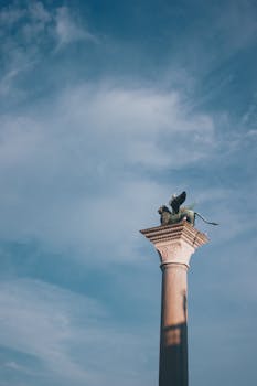 Iconic St. Mark's Winged Lion stands atop a column against a clear blue sky in Venice, Italy.