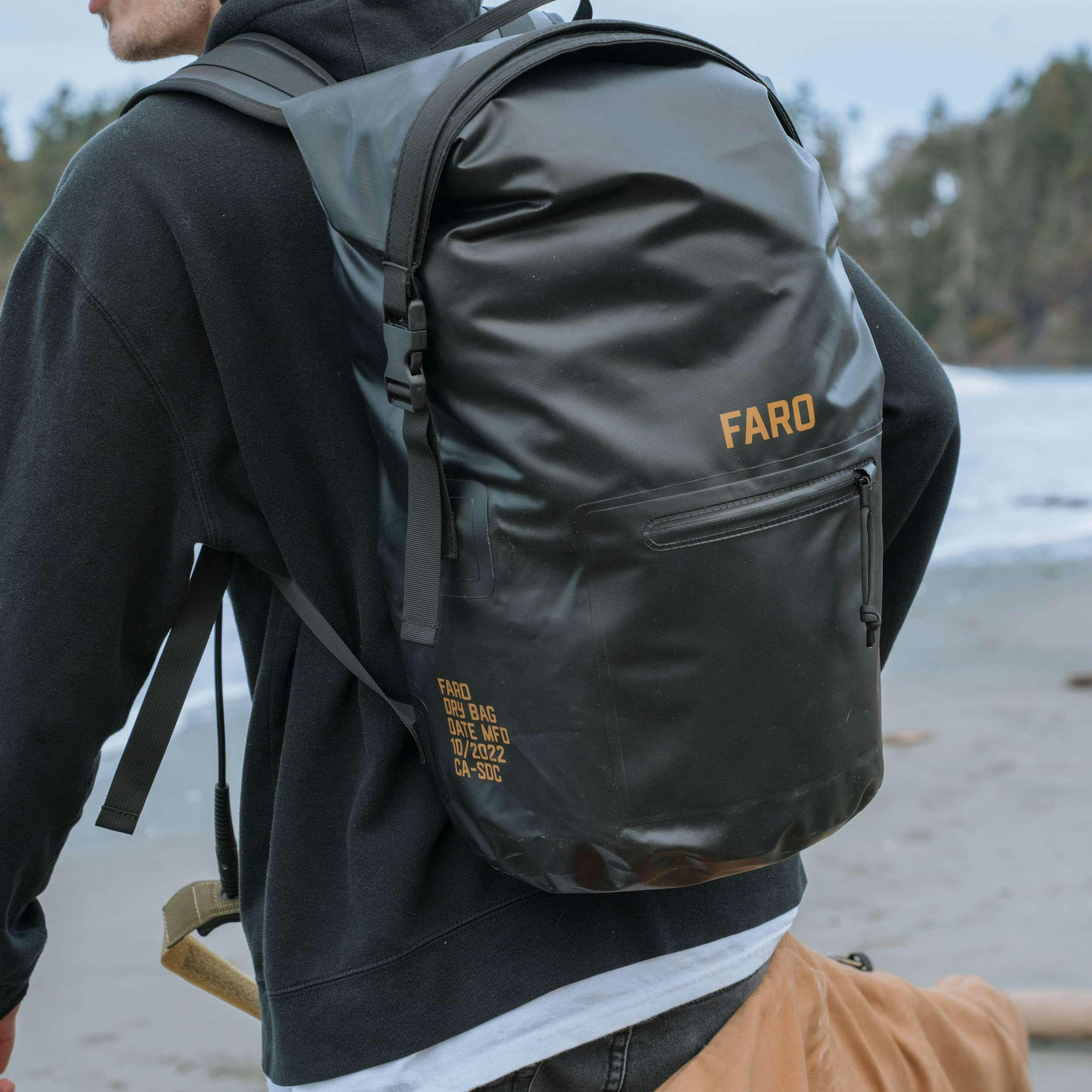Man wearing a black waterproof backpack on a scenic beach, ready for adventure.