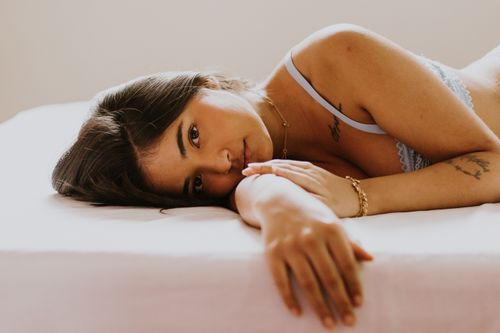 Free Close-up portrait of a woman in lingerie resting on a bed with tattoos visible. Stock Photo