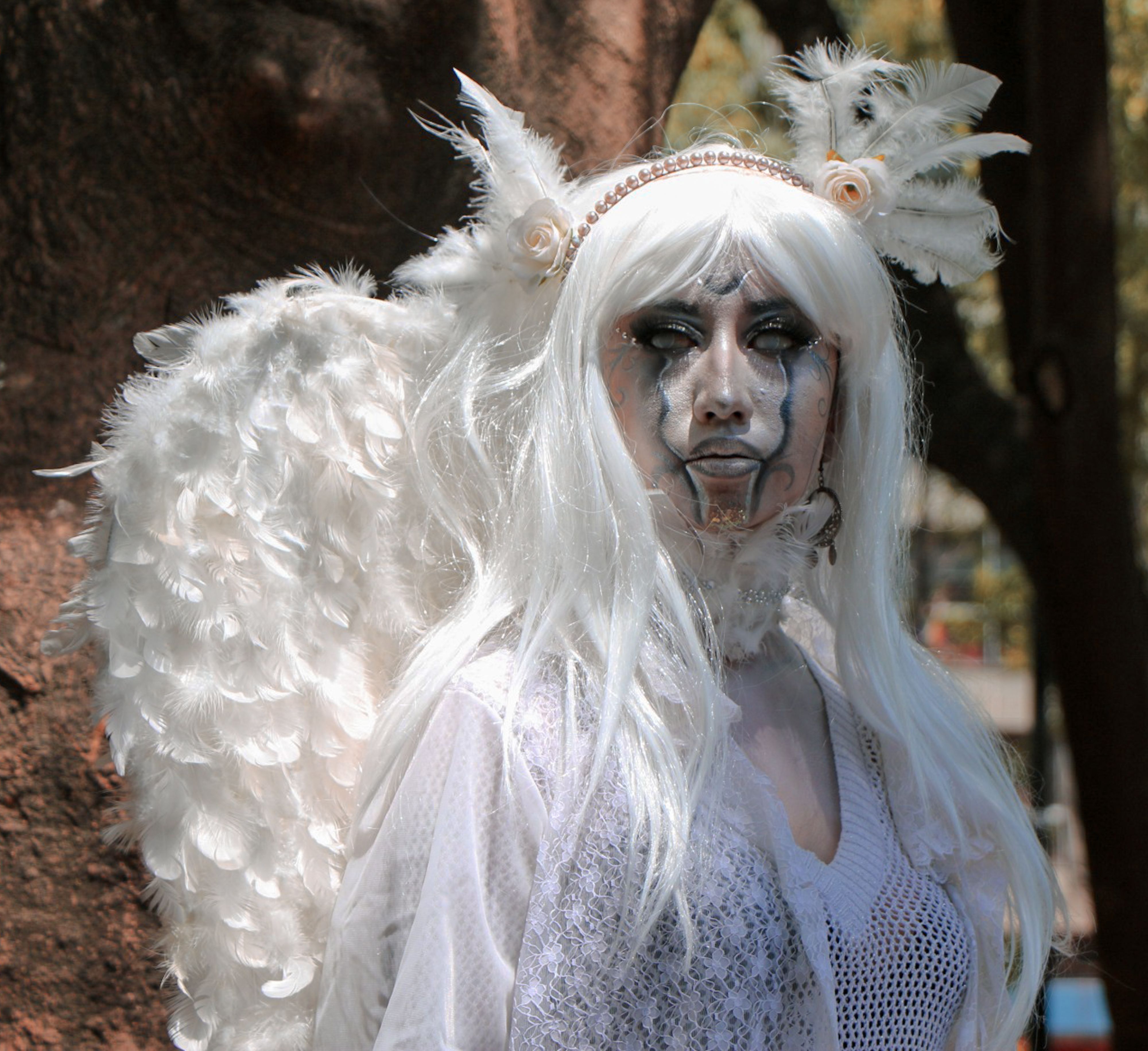 A striking portrait of a person in an ethereal angel costume with dramatic makeup outdoors.