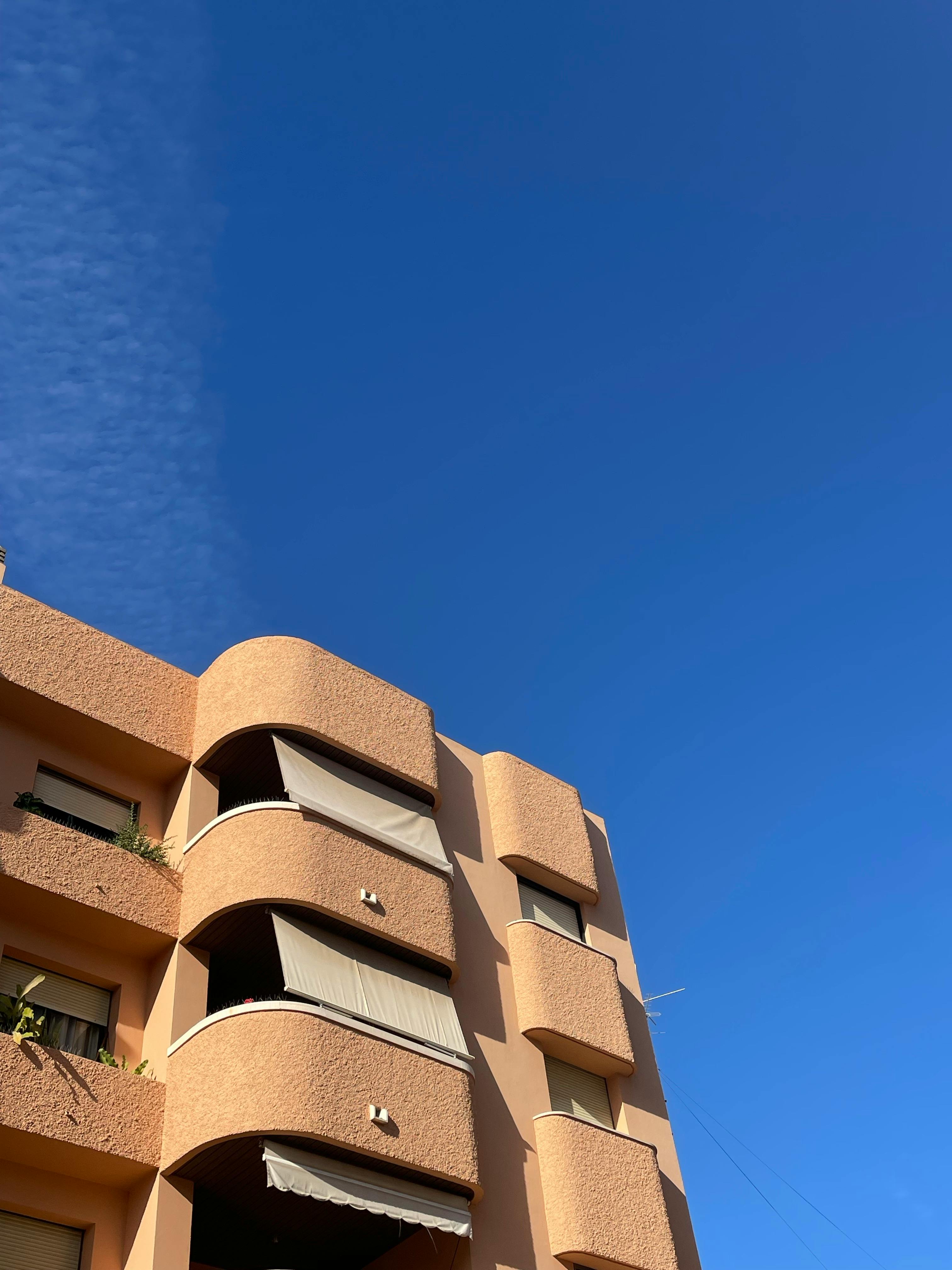 Low angle view of a modern apartment building with brown facade and clear blue sky.