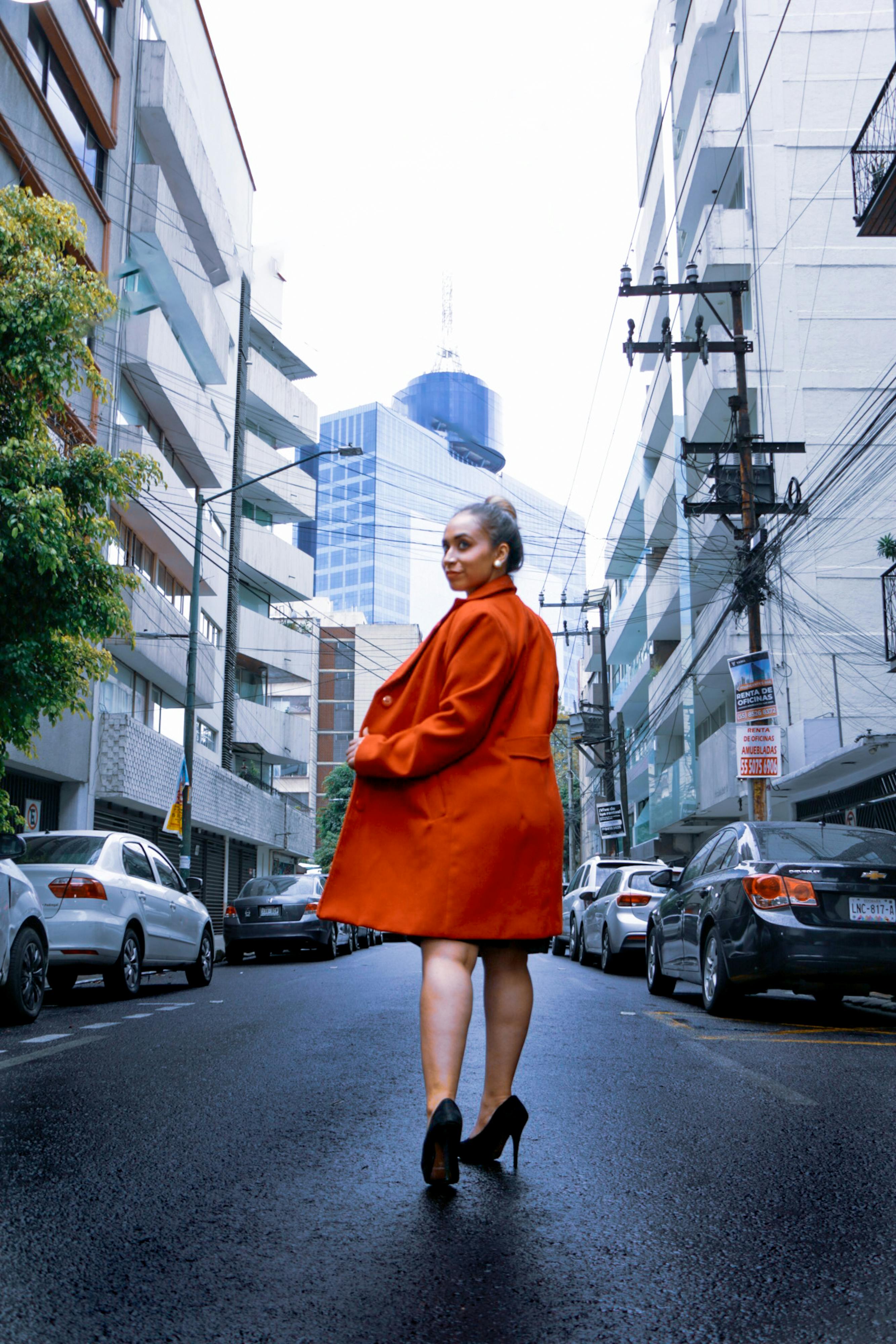 Woman in red coat confidently walking in an urban street, fashion statement.