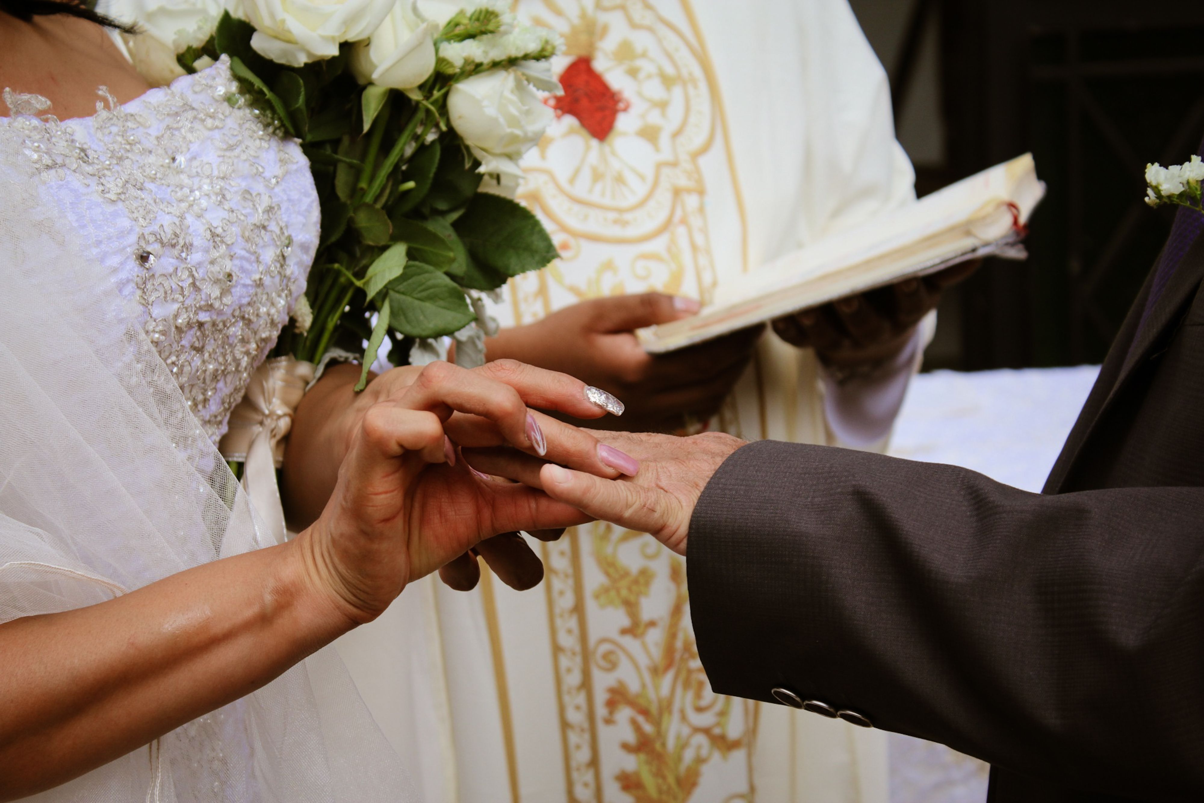 Close-up of a bride and groom exchanging rings during a wedding ceremony with a priest.