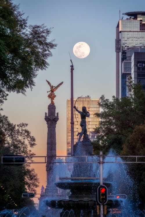 A full moon rises over a fountain and statue