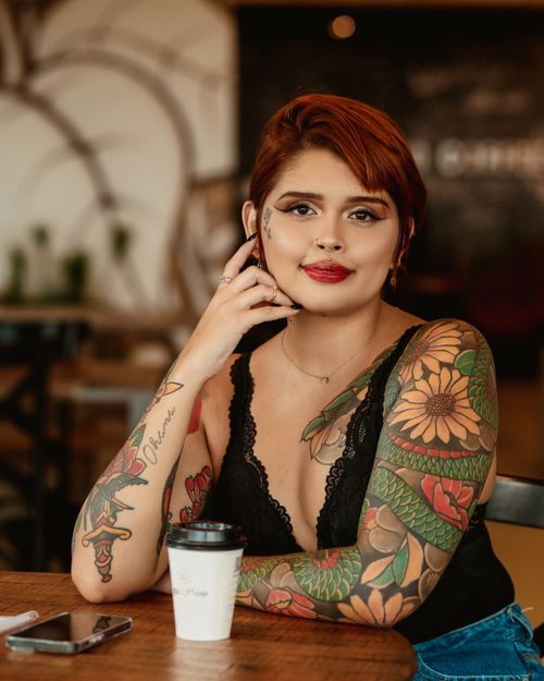 Free A tattooed woman with short hair enjoying coffee at a cafe. Vibrant tattoos and fashion style depicted. Stock Photo