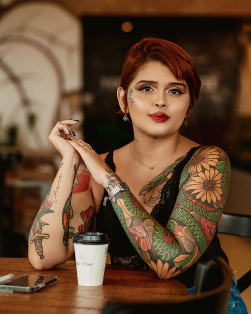 Free A fashionable woman with tattoos enjoys a drink in a cozy café. Perfect for lifestyle and fashion themes. Stock Photo