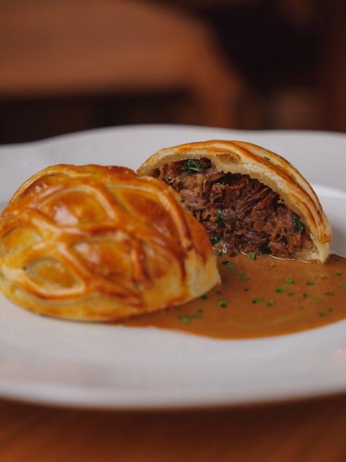 Free Mouth-watering beef Wellington with sauce garnished with herbs on a plate, perfect for gourmet lovers. Stock Photo